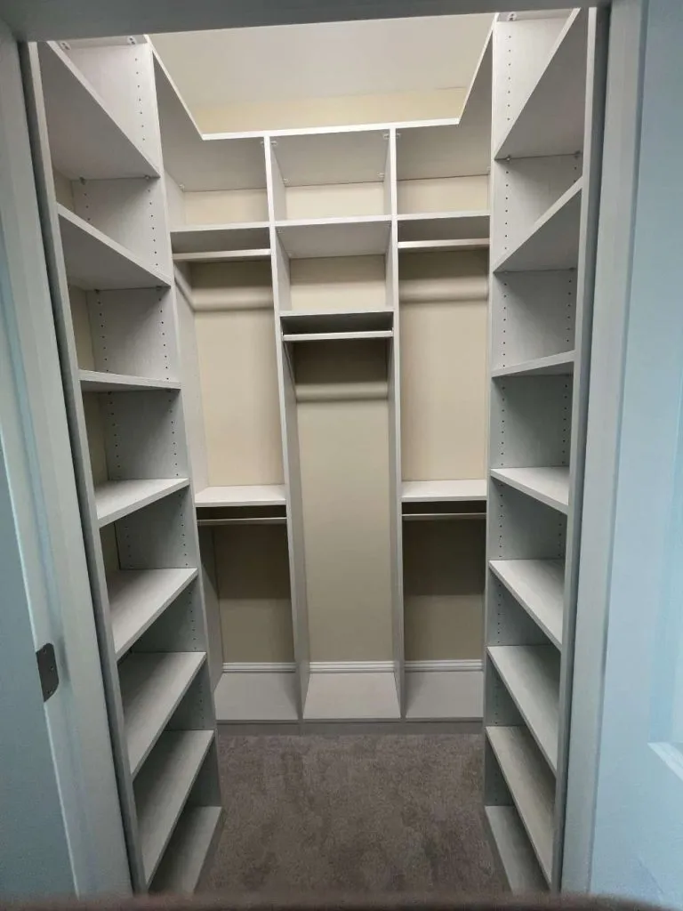 Narrow walk in closet with angled shelves on both sides and double hanging rods in the center